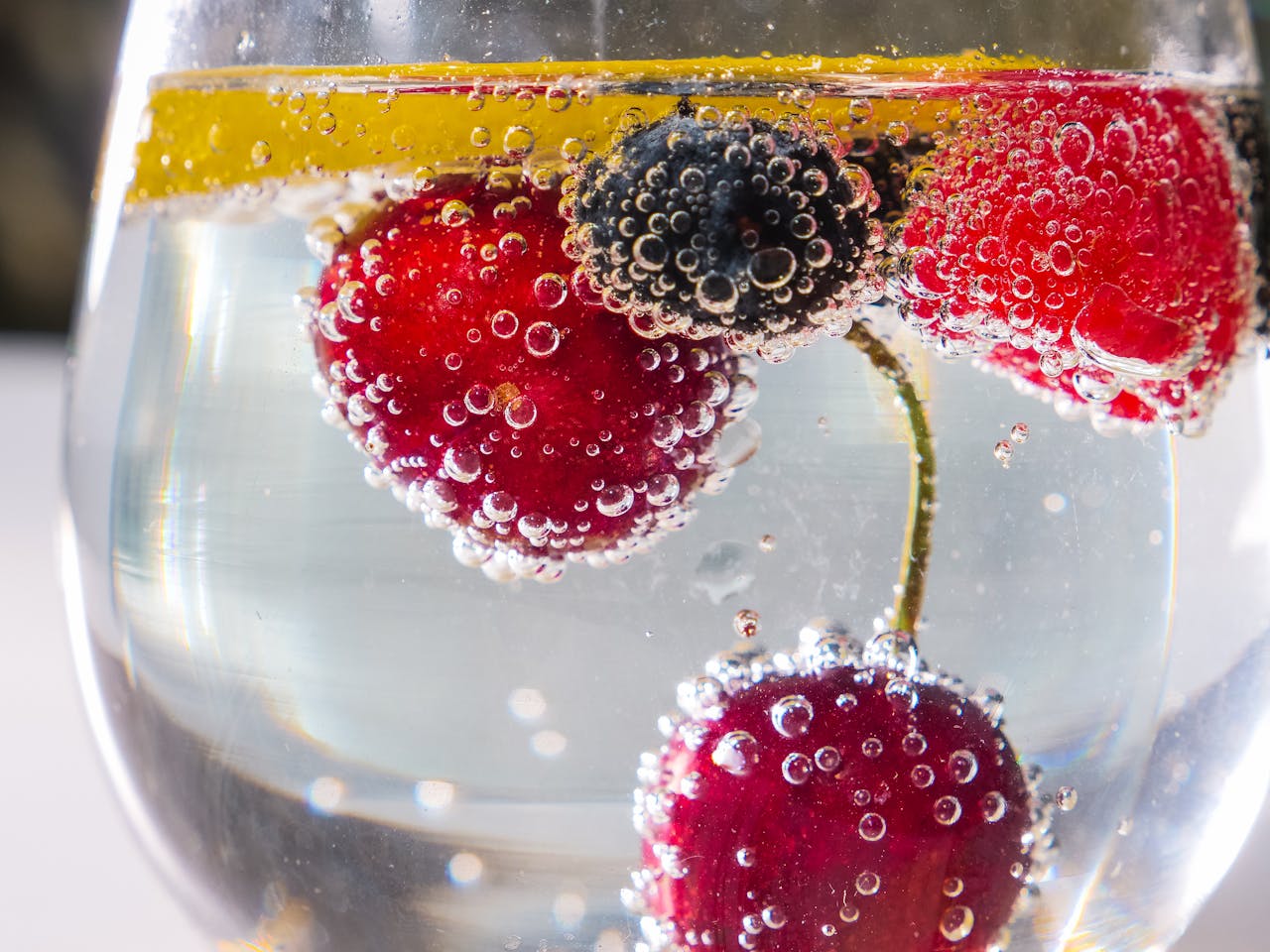 services-02 Close-up of fresh berries and lemon slice in sparkling water with bubbles.
