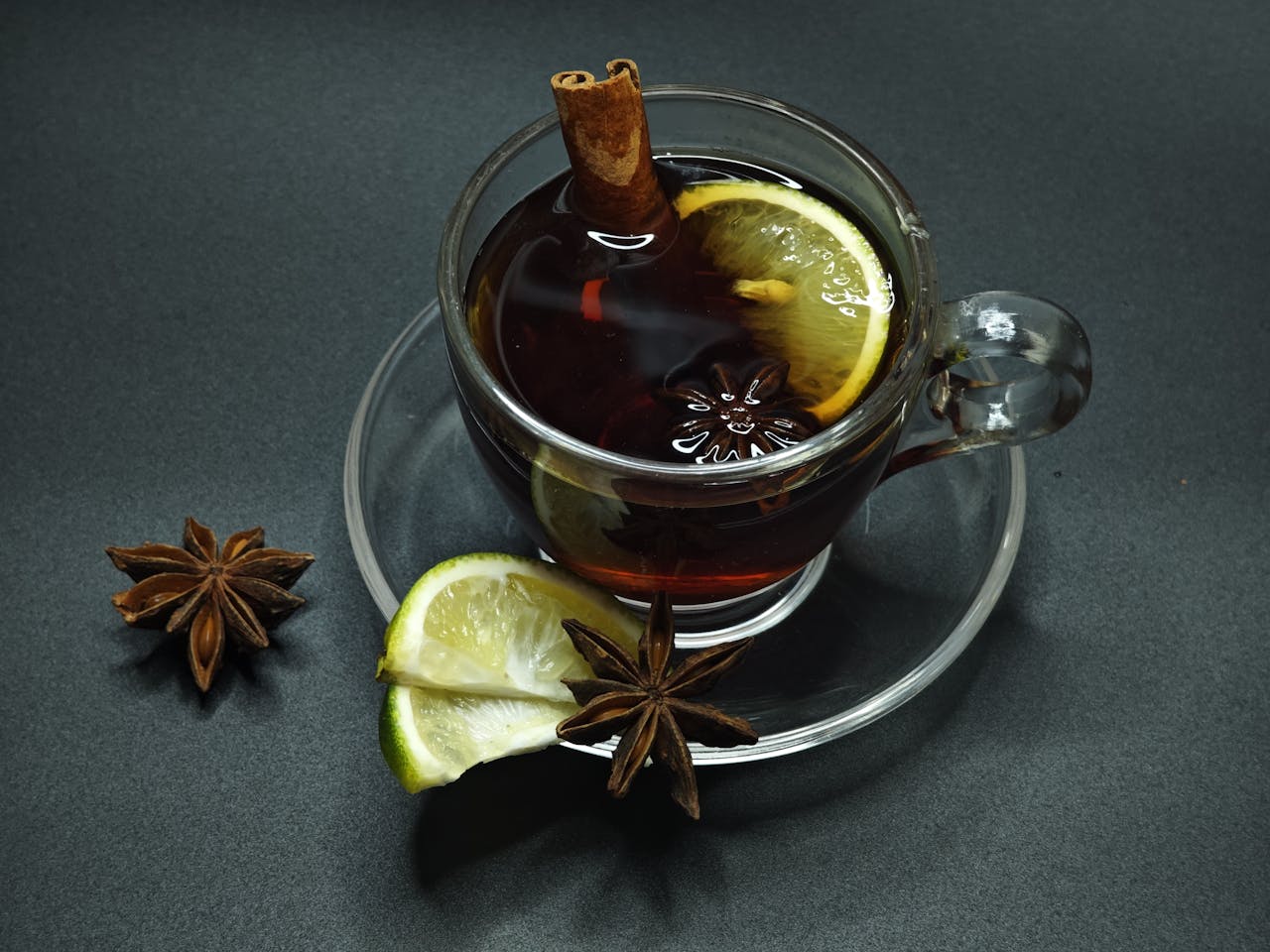 Glass of spiced tea with lemon slice, cinnamon stick, and star anise on a dark background.