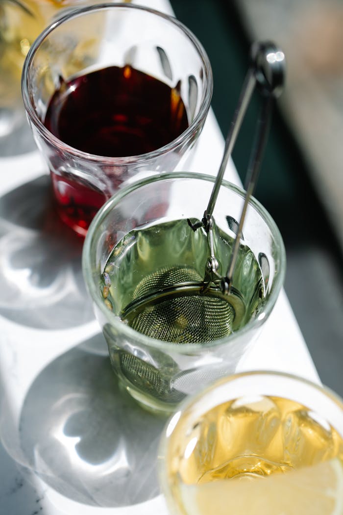 services-04 Three glasses of colored tea with a metal infuser in bright sunlight.