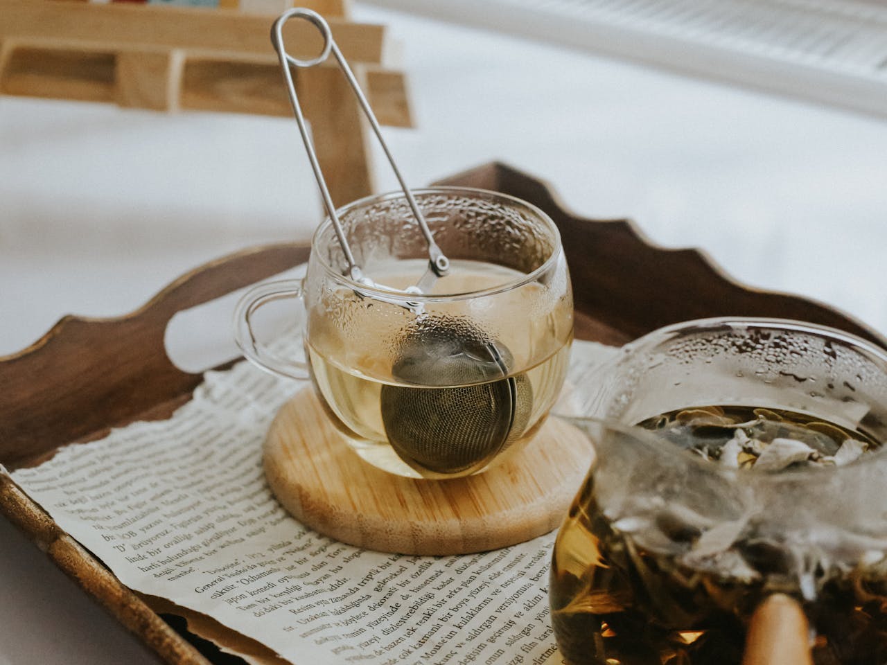 about-01 A warm, cozy scene showcasing glass teacups with tea infuser on a tray with scattered papers.